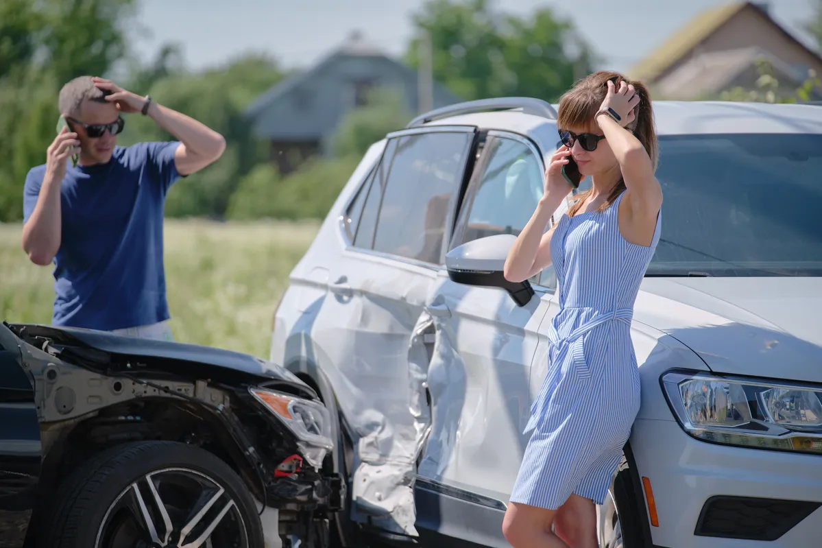 araffe woman in a blue dress talking on a cell phone next to a wrecked car