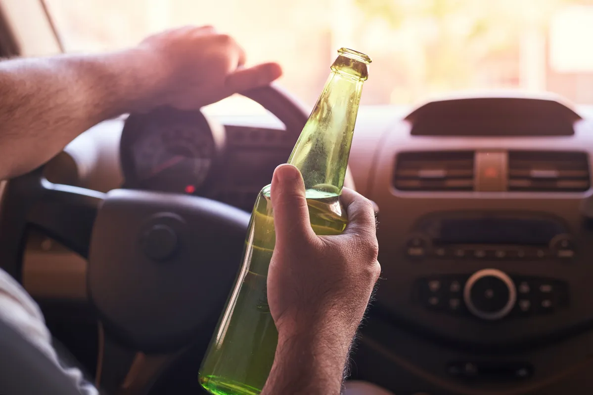 someone holding a bottle of beer in their hand while driving a car